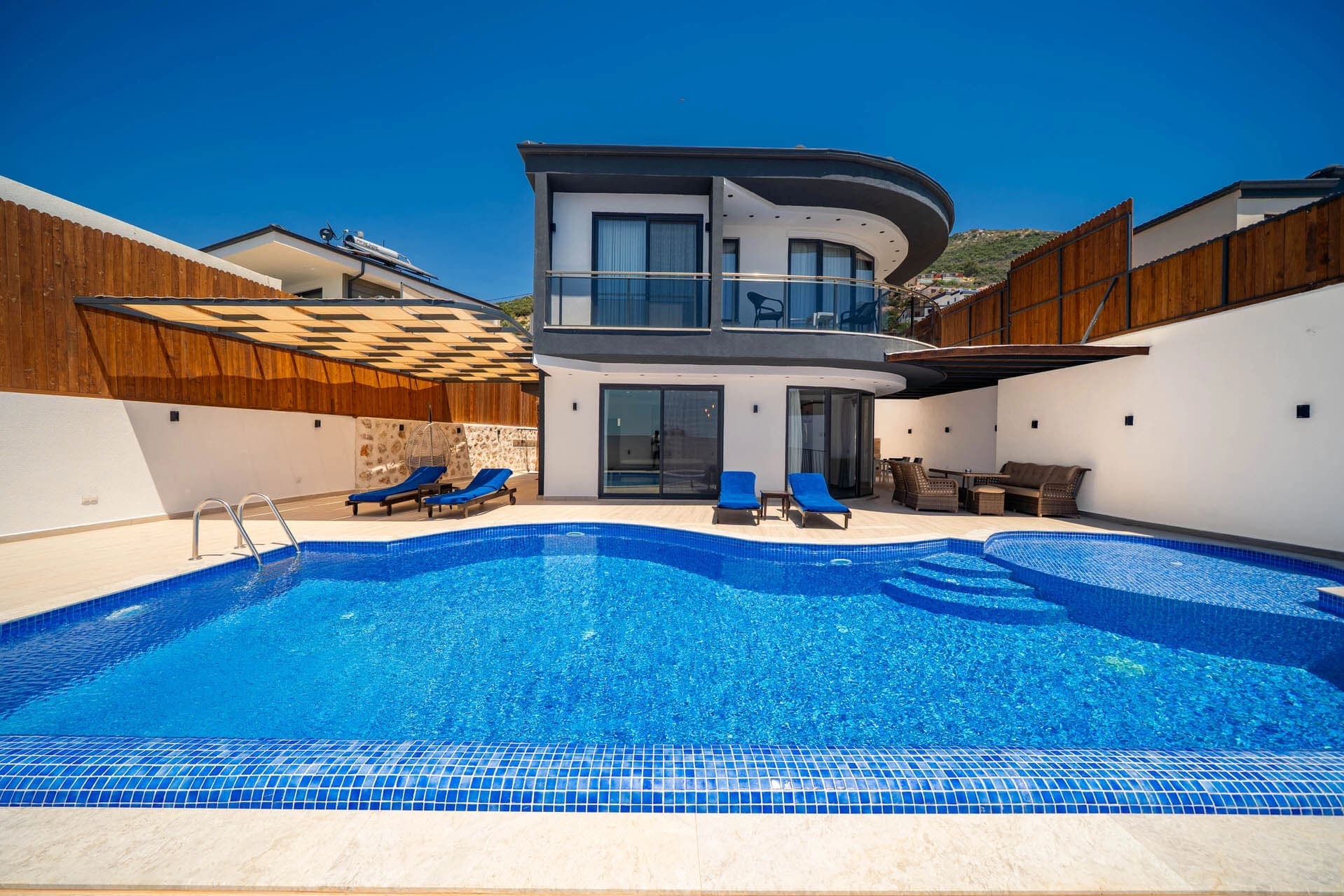 Önünde yüzme havuzu ve şezlonglar bulunan iki katlı modern villa.