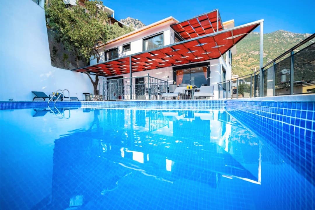 Güneşlik tente altındaki terası ve mavi havuzu olan iki katlı villa.
