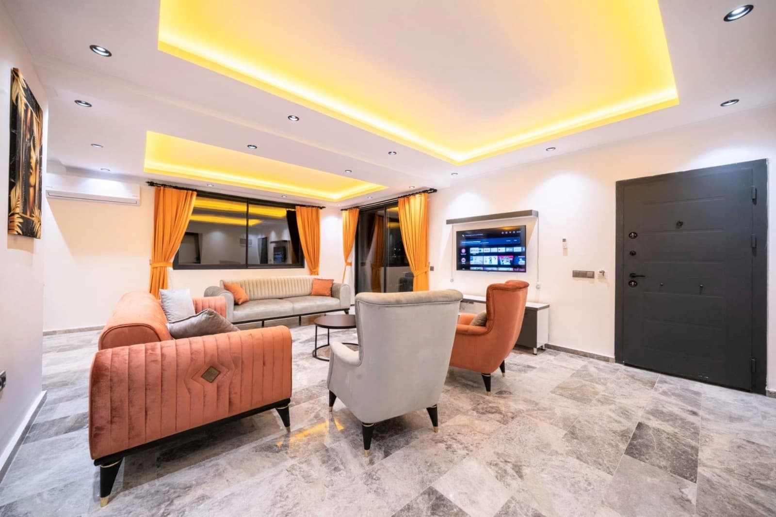 Salon içerisinde kiremit rengi koltuklar, gri berjerler ve sarı LED aydınlatmalı tavan yer alıyor.