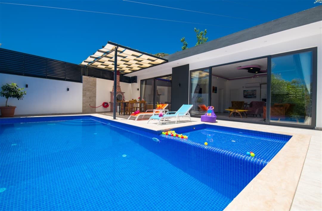 Mavi havuzlu, şezlonglu, gölgelikli ve barbekü alanı bulunan modern villanın terası.