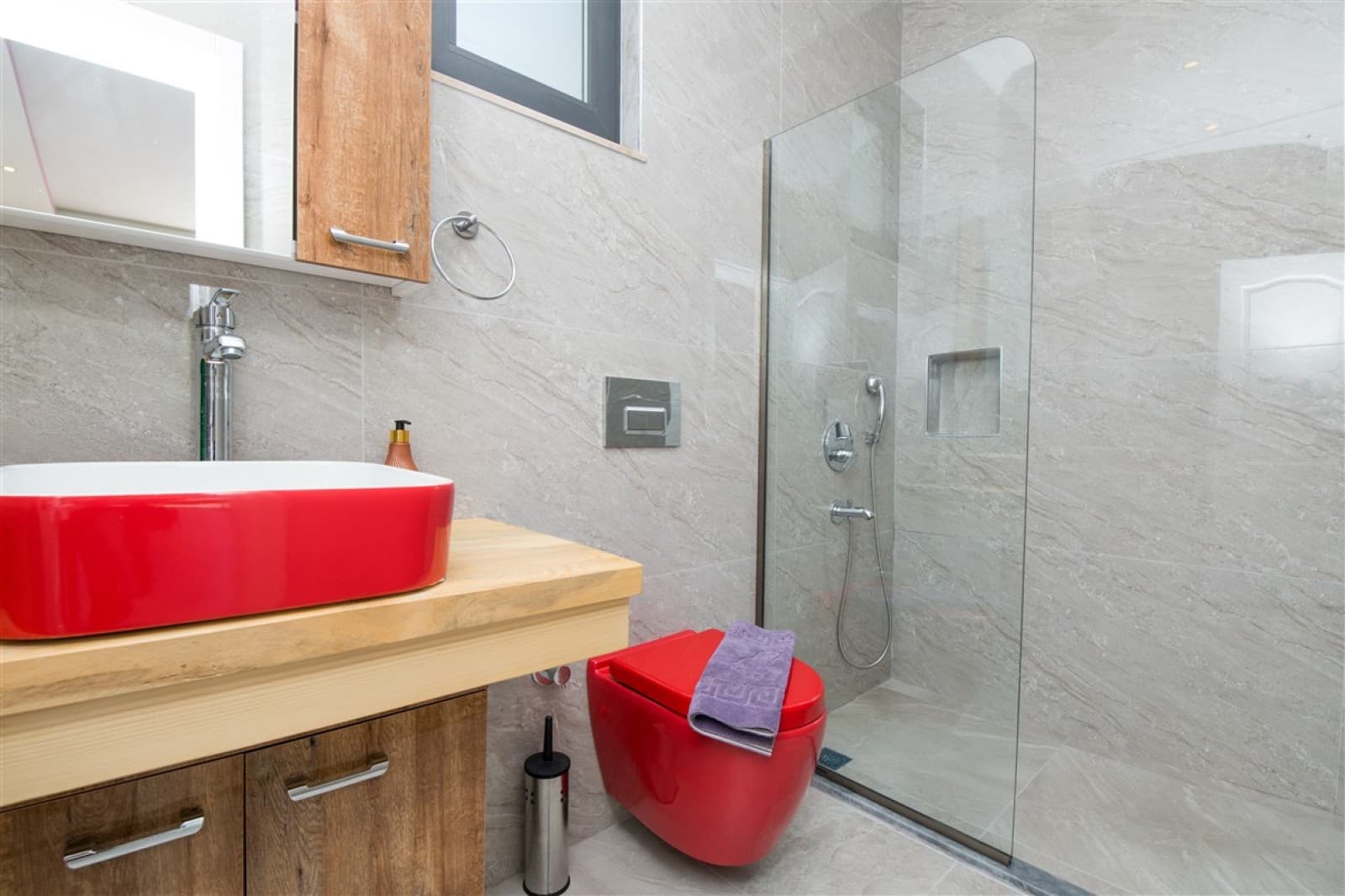 Gri seramik kaplı banyoda kırmızı lavabo ve kırmızı klozet bulunuyor.