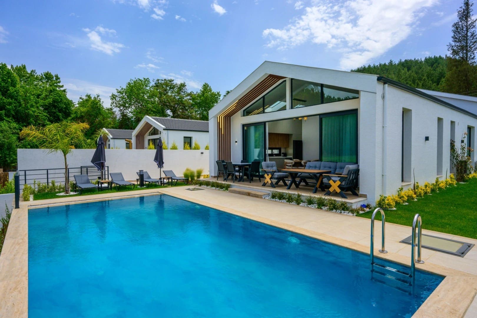 Bahçesinde yüzme havuzu ve oturma grubu bulunan beyaz villa.