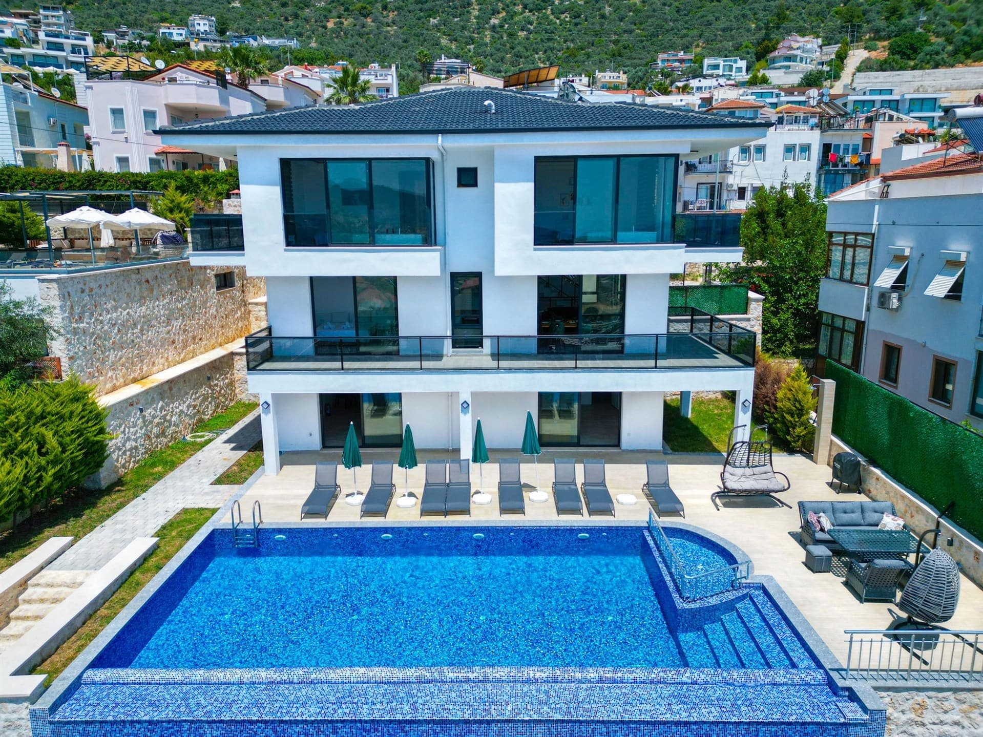 Önünde yüzme havuzu ve şezlonglar bulunan, çok katlı ve beyaz cepheli modern villa dış görünümü.