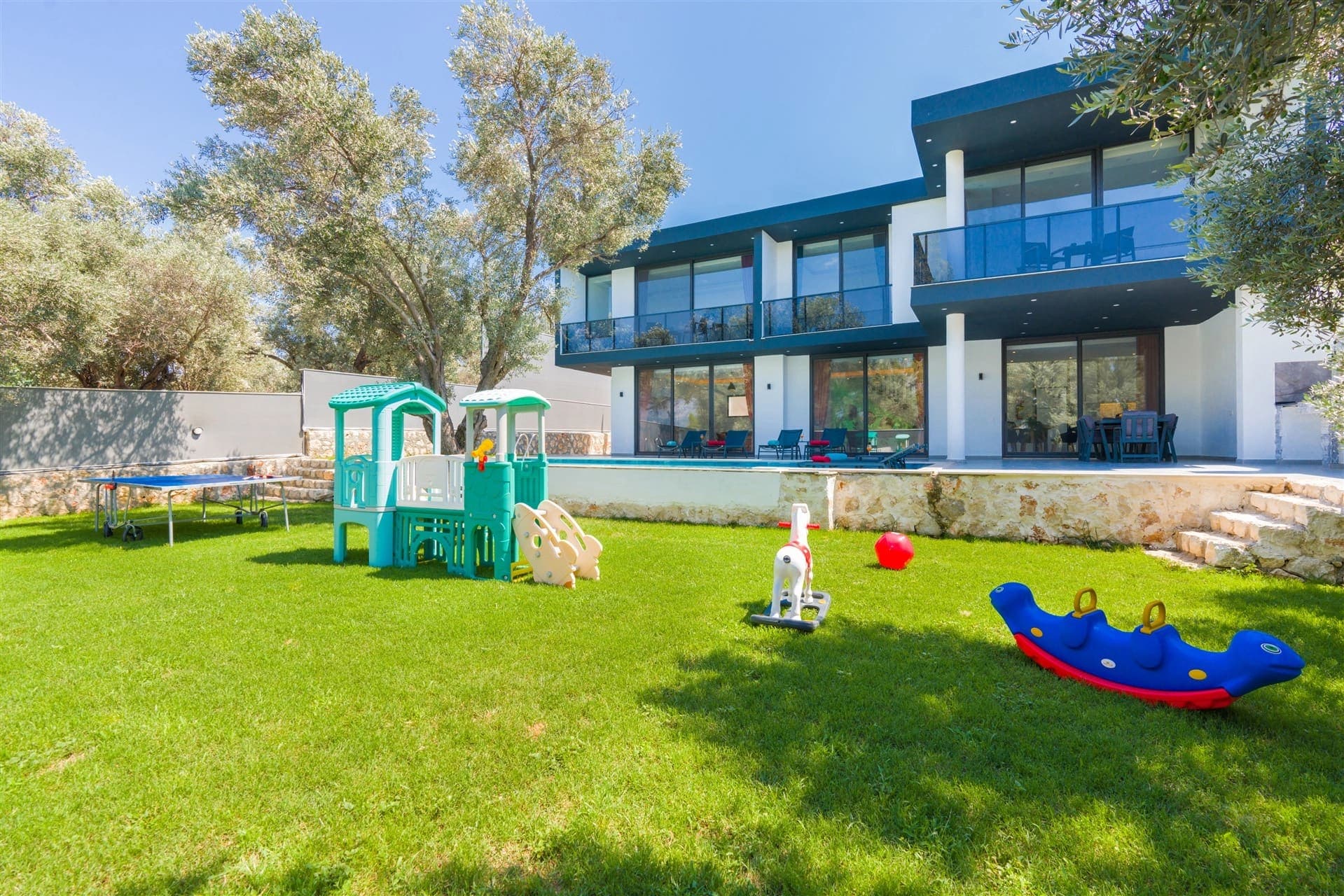 Çim bahçede çocuk oyun parkı ve arkasında modern iki katlı villa.