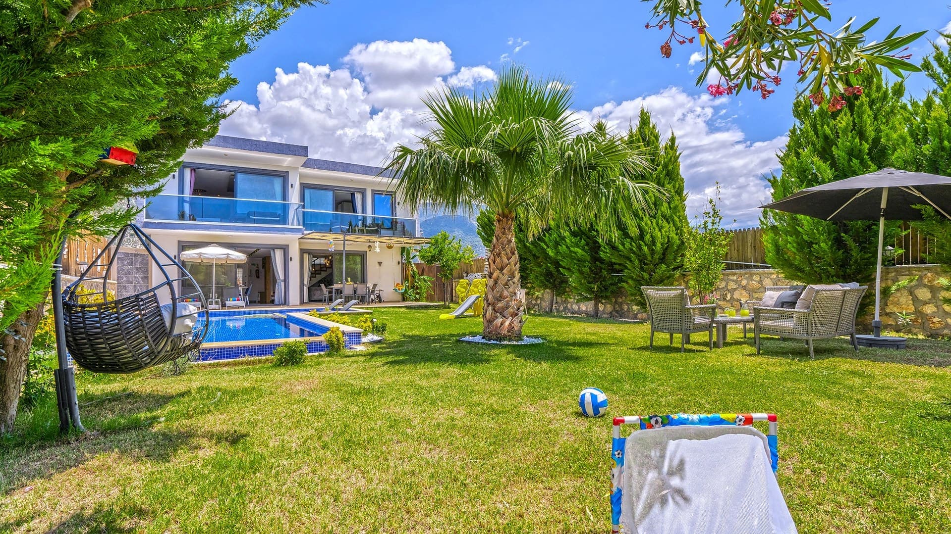 Palmiyeli yeşil bahçe içinde iki katlı villa ve havuz.