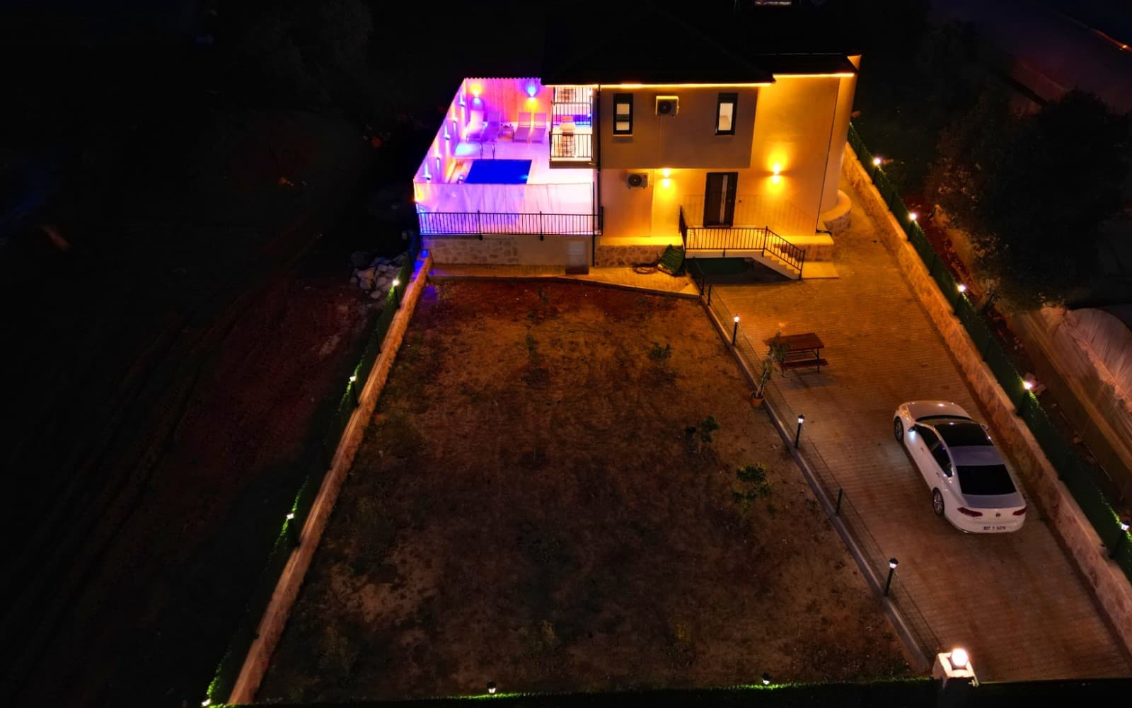 Gece havadan çekilen villanın dış cephesi ve aydınlatılmış havuz alanı.