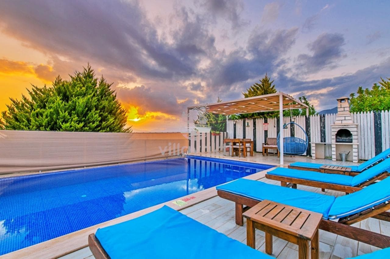 Gün batımı manzarasında havuz kenarındaki şezlonglar ve ahşap pergola dikkat çekiyor.