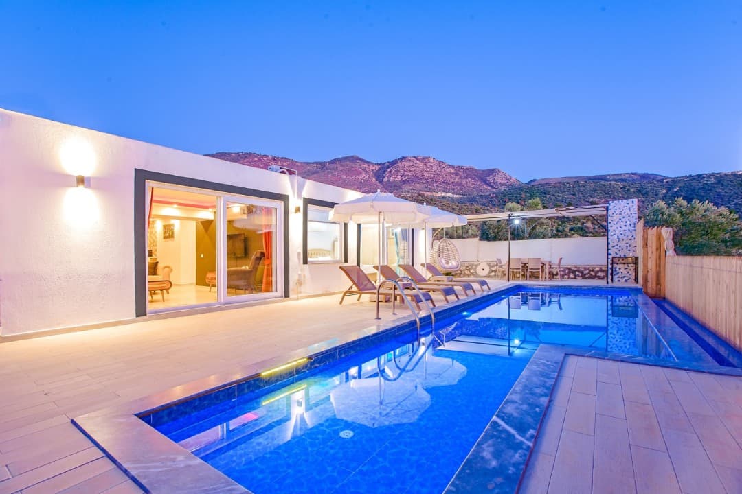 Akşam vakti havuz başı şezlongları ve dağ manzaralı tek katlı beyaz villa.