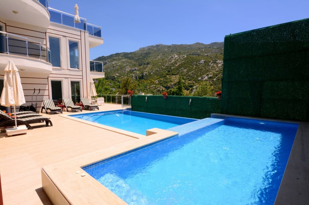 Dağ manzaralı havuz kenarında şezlonglar bulunan iki katlı villa.