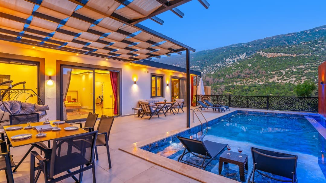 Dağ manzaralı terasta havuz, yemek masası ve gölgelikli oturma alanı bulunan villa.
