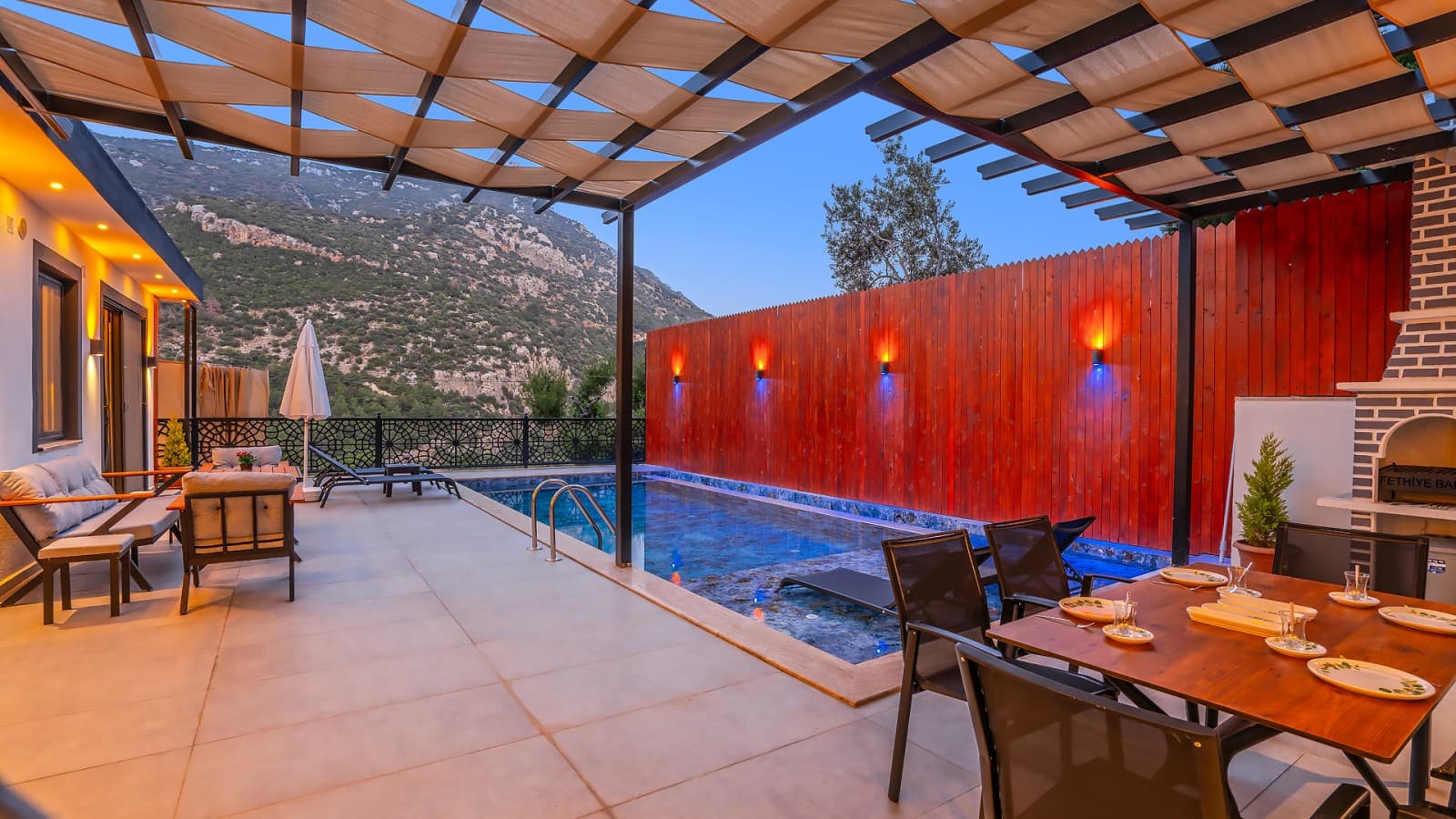 Pergola altındaki yemek masası ve ışıklandırmalı havuz.