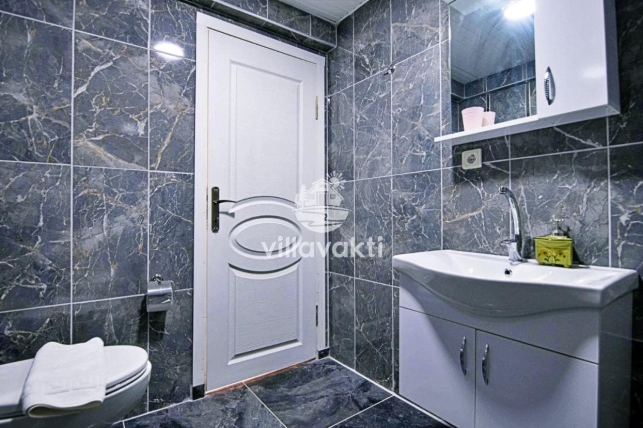 Mavi mermer kaplı duvarları olan banyoda beyaz lavabo, dolaplı ayna ve duş kapısı yer alıyor.
