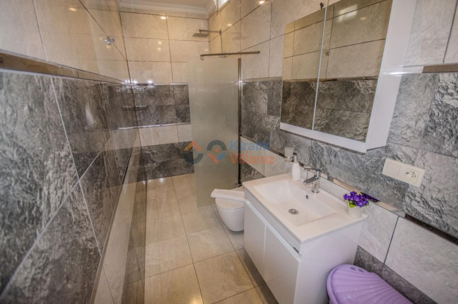Gri mermer kaplı modern banyo, cam duşakabin ve beyaz lavabo.