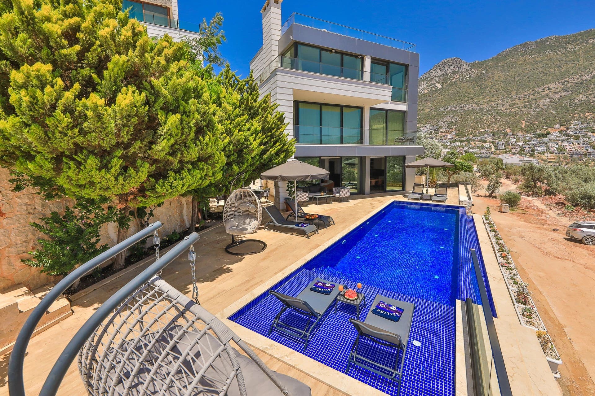 Yemyeşil ağaçların yanında uzun havuzu bulunan modern villa.