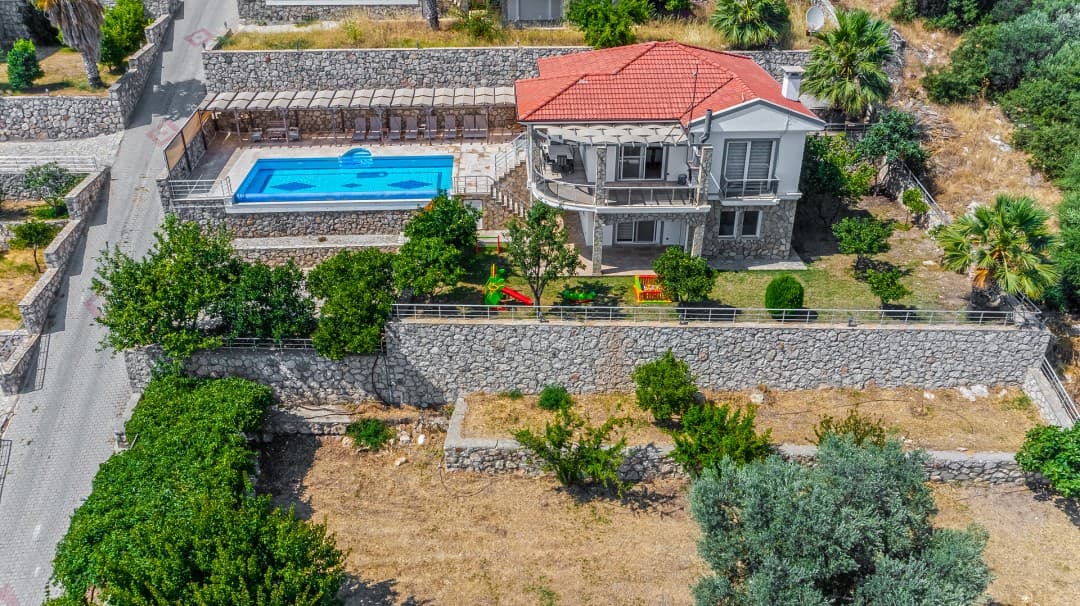 Havuzlu ve kiremit çatılı iki katlı villanın havadan görünümü.