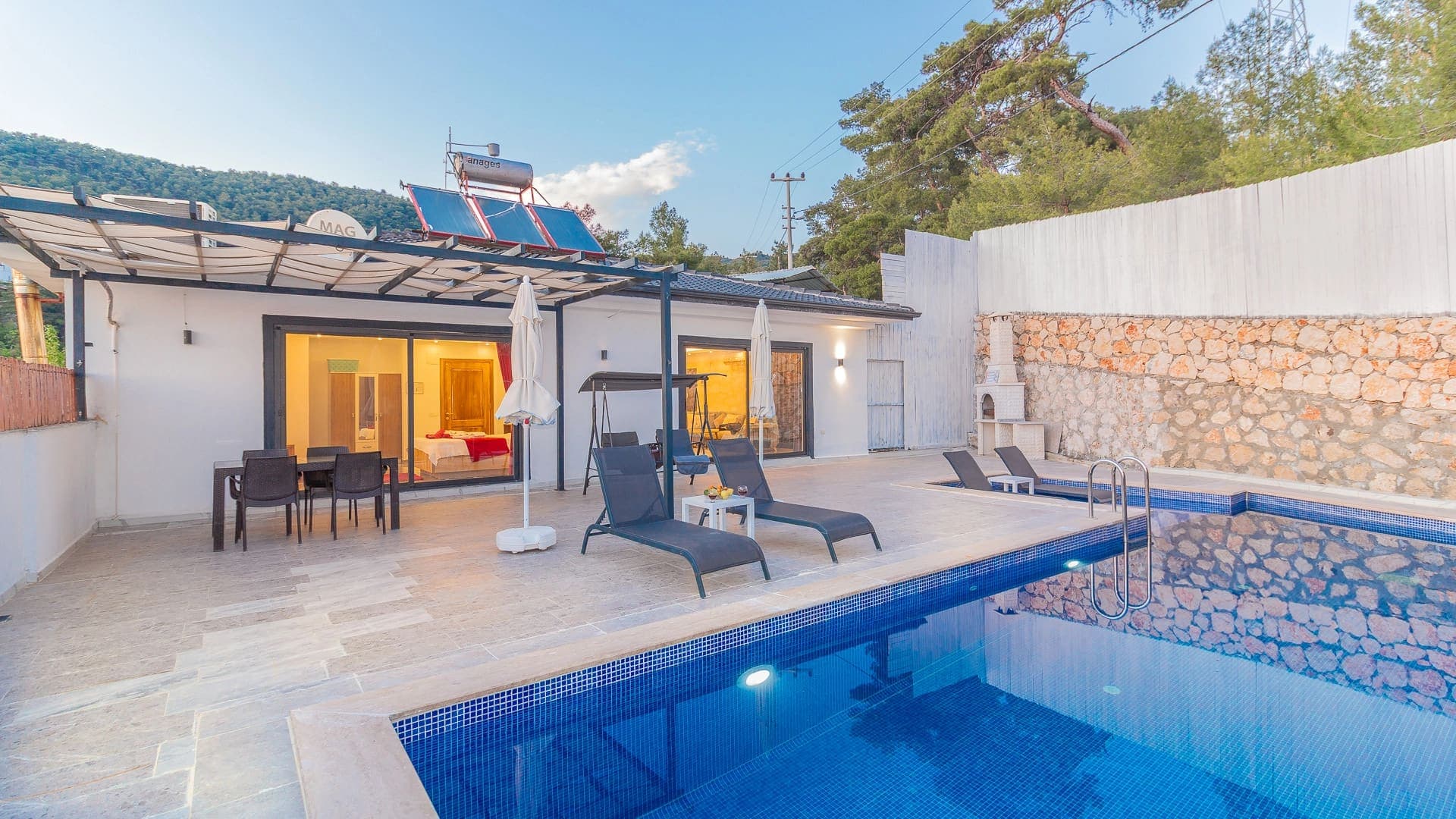 Mavi havuz kenarında şezlonglar ve arka planda orman manzaralı villa.