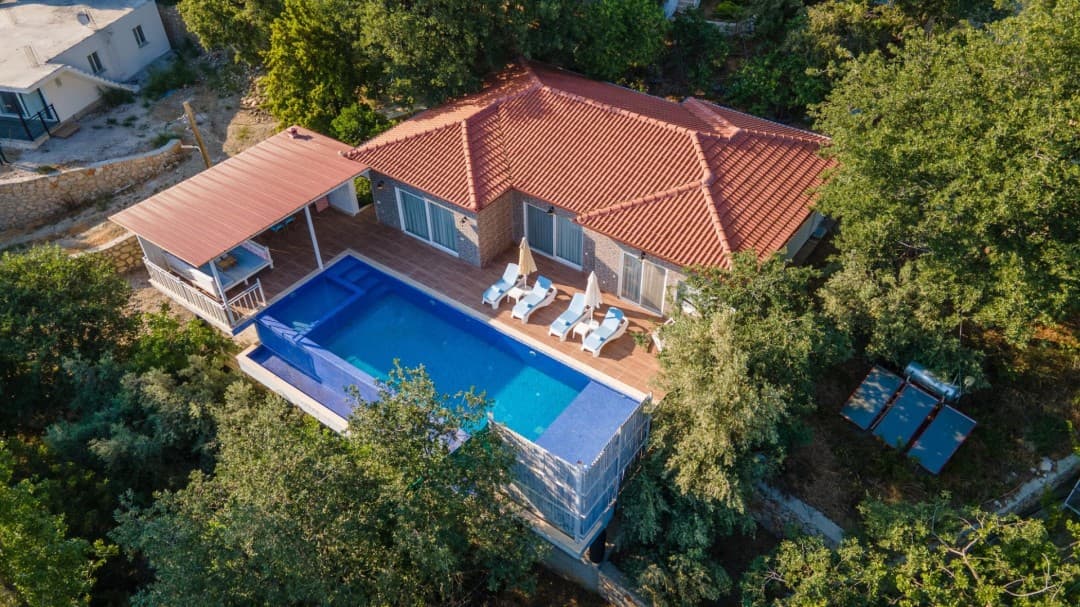 Kiremit çatılı tek katlı villanın havuzu ve şezlonglu ahşap terası.