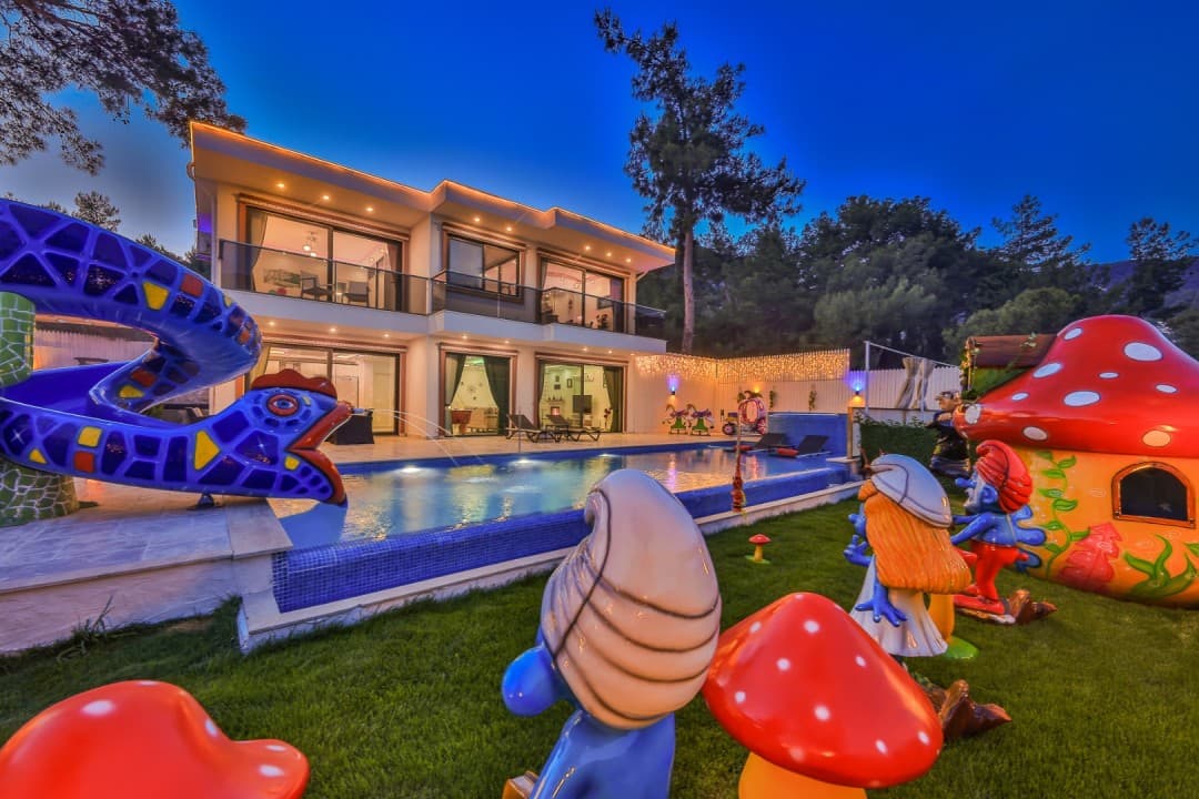 Akşam ışıklandırmalı, havuzlu, kaydıraklı ve Şirinler temalı bahçe süsleri bulunan iki katlı modern villa.