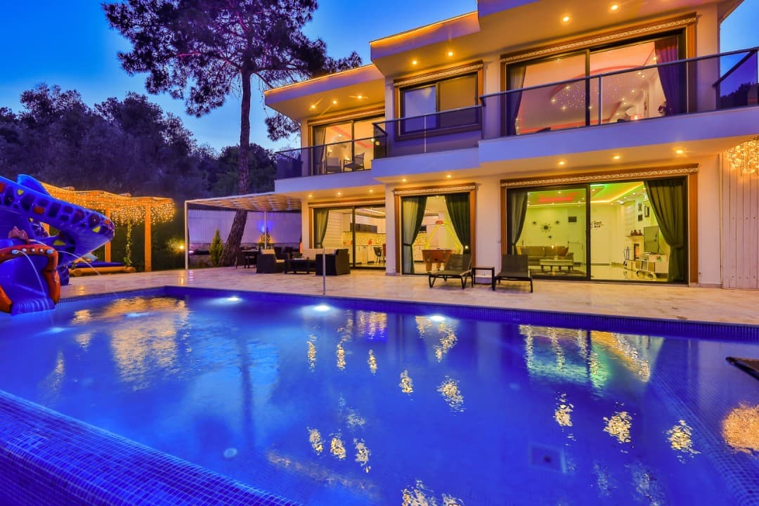 Işıklandırmalı iki katlı villa ve önündeki havuz.
