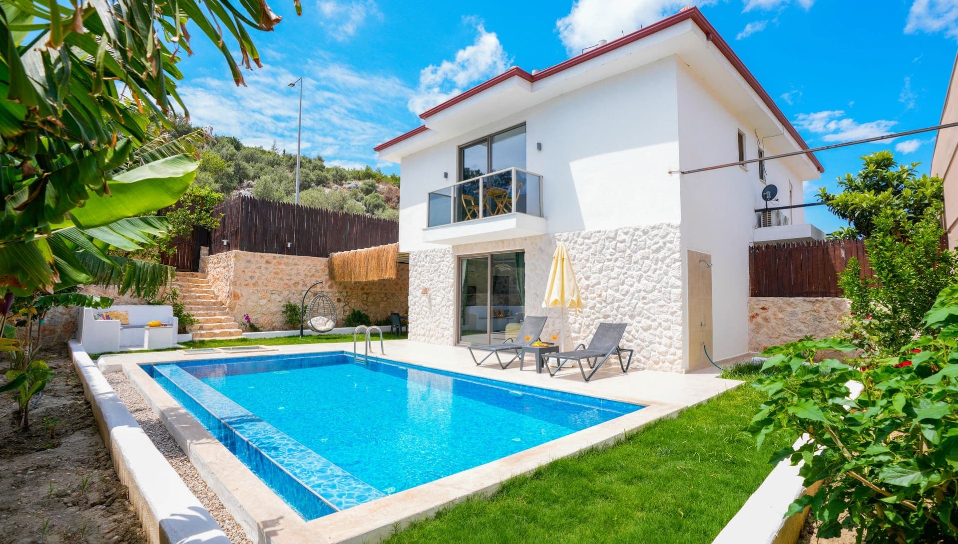 Bahçesinde havuz ve şezlonglar bulunan iki katlı beyaz villa.