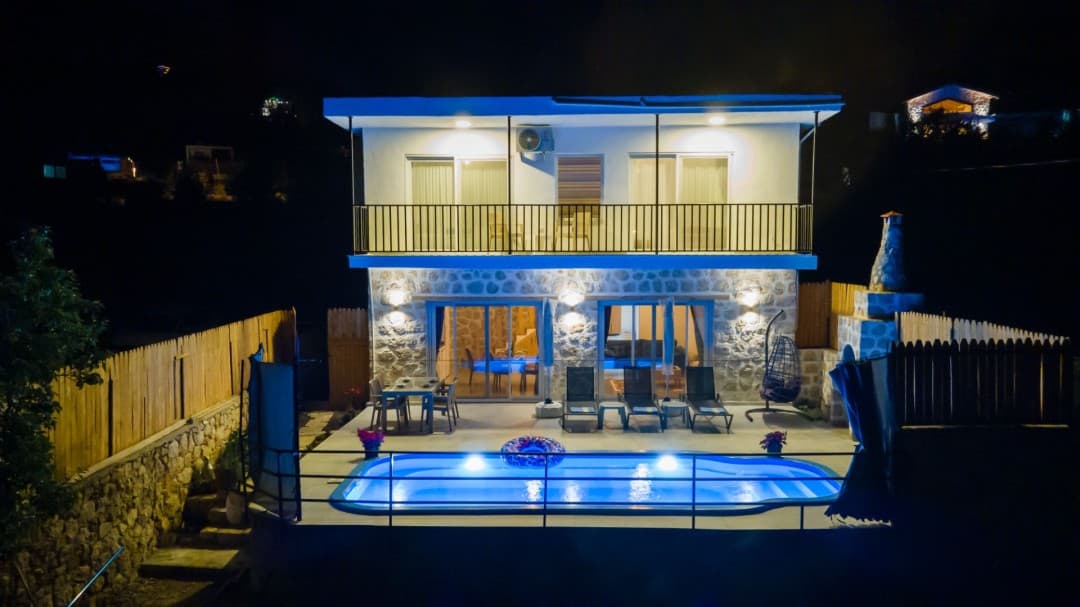 Gece aydınlatmalı havuzu, şezlongları ve taş kaplama dış cephesiyle iki katlı müstakil villa.