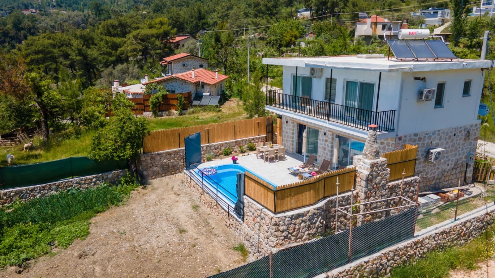 Taş kaplamalı iki katlı villa ve önünde havuz bulunan bahçe.