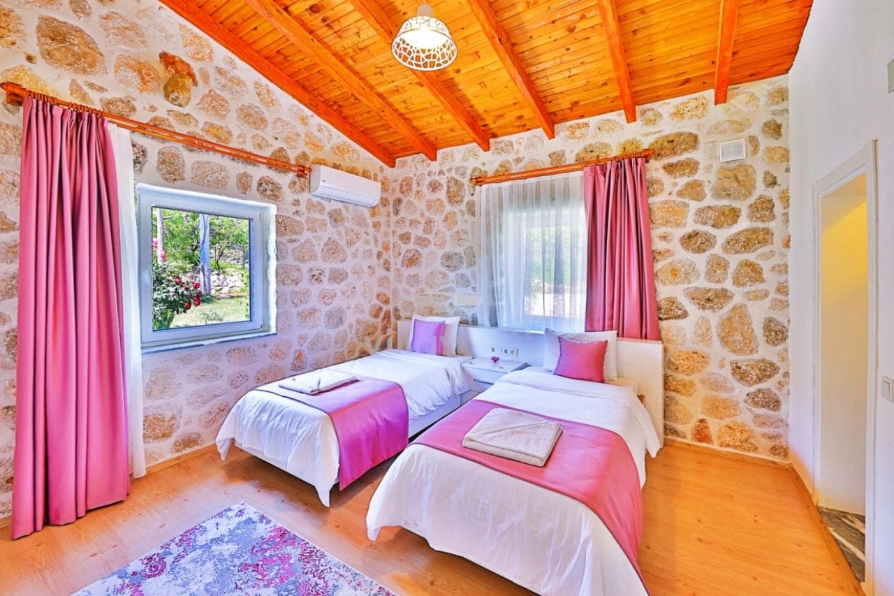 Pembe detaylı iki yataklı taş duvarlı yatak odası.