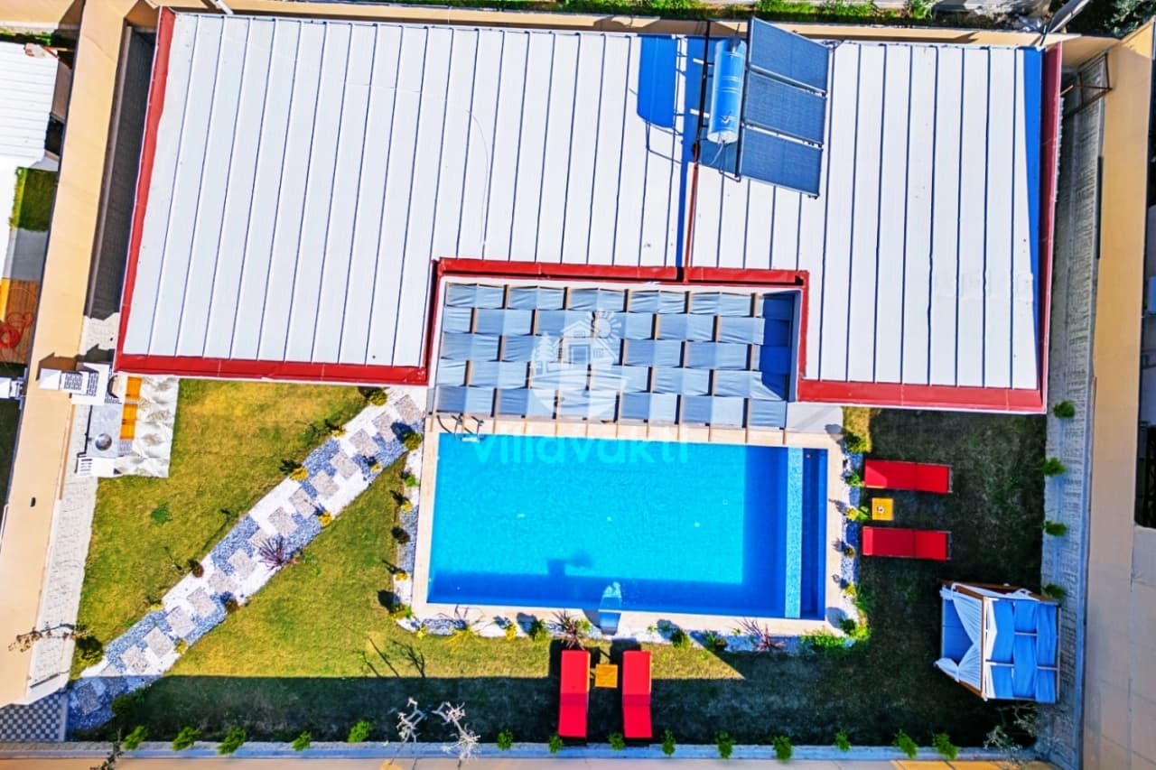 Çatısı metal panelli villanın havuzu, şezlongları ve çimenlik bahçesi.