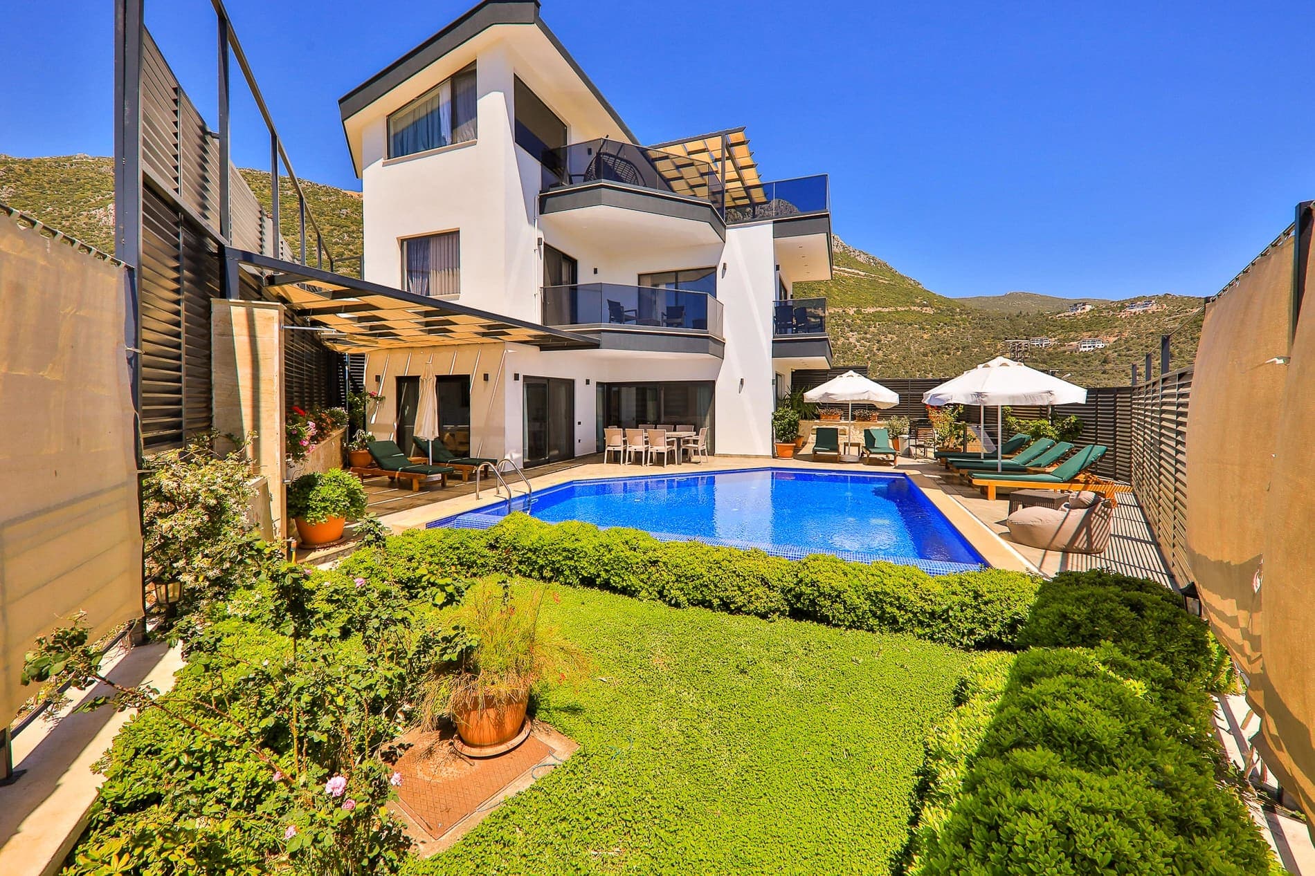 Yemyeşil bahçesi ve şezlongları olan havuzlu villa dış cephesi