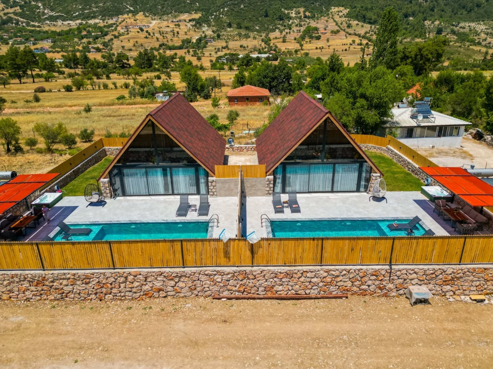 Doğa manzaralı, üçgen çatılı ikiz villaların havuzlu ve şezlonglu dış cephe görünümü.