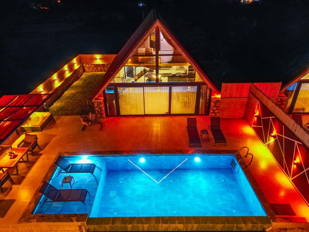 Gece aydınlatmalı havuzu, şezlongları ve üçgen çatılı yapısıyla havuzlu villa.
