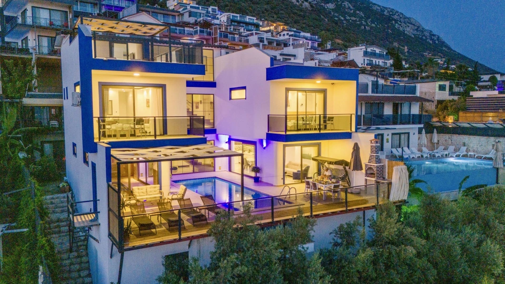 Akşam vakti aydınlatılmış mavi detaylı modern villa ve havuz katı.