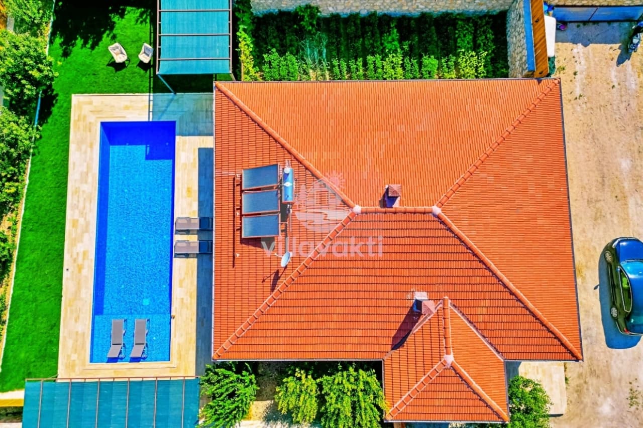 Kiremit çatılı evin havuz ve yeşil bahçesinin havadan görünümü.