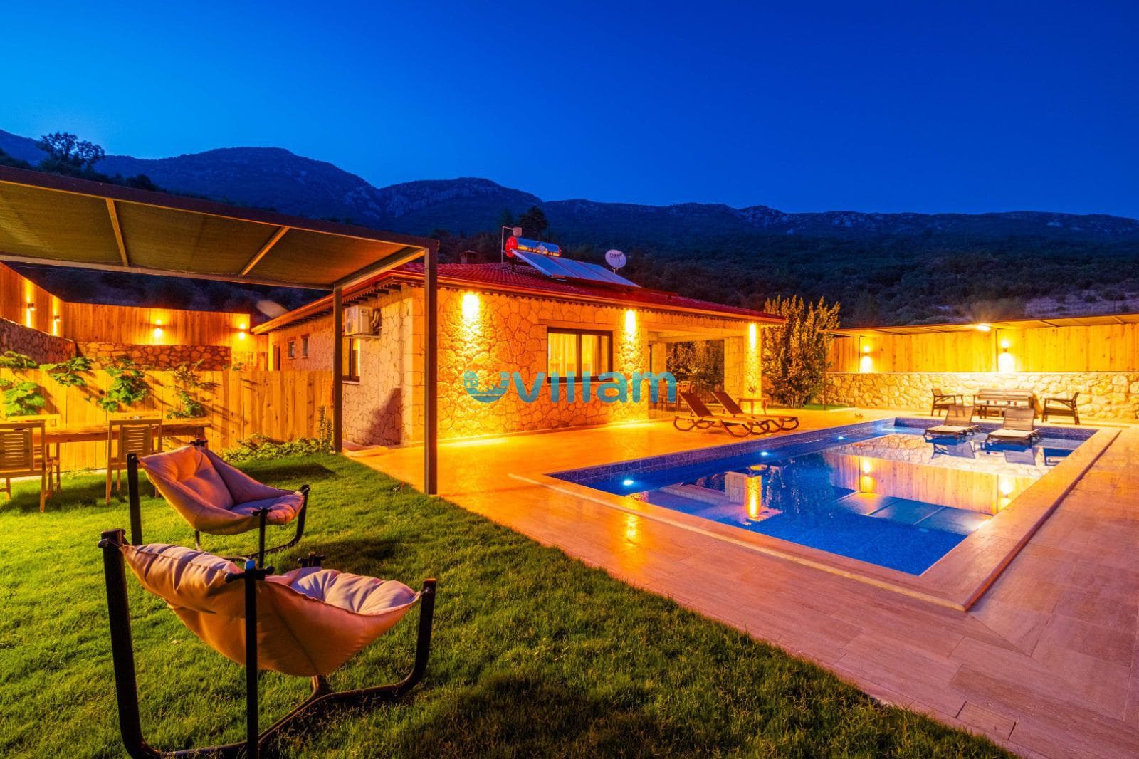 Akşam aydınlatmasında taş duvarlı tek katlı havuzlu villa.