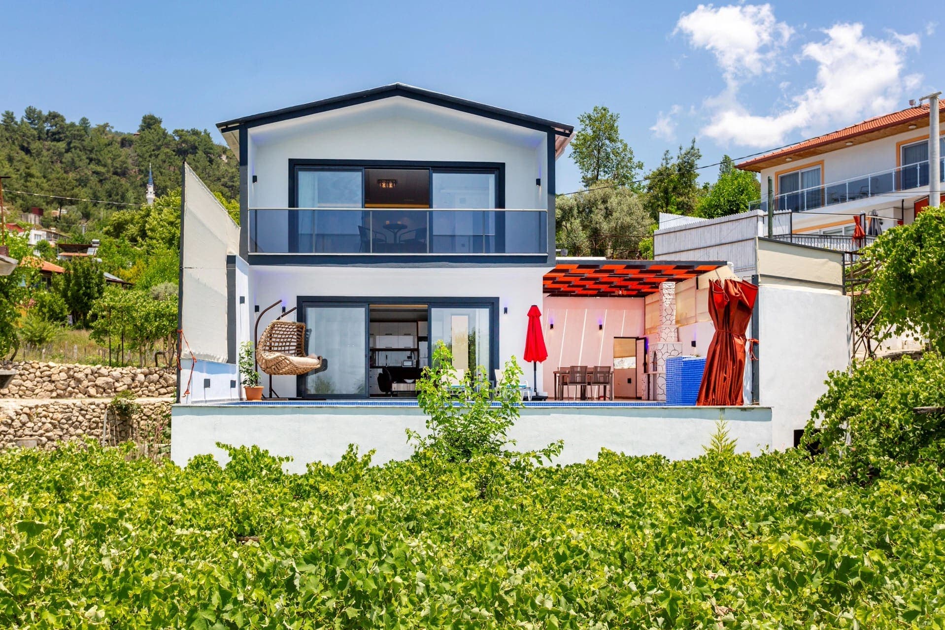 Yeşillikler arasında yer alan iki katlı modern villanın ön cephesi.