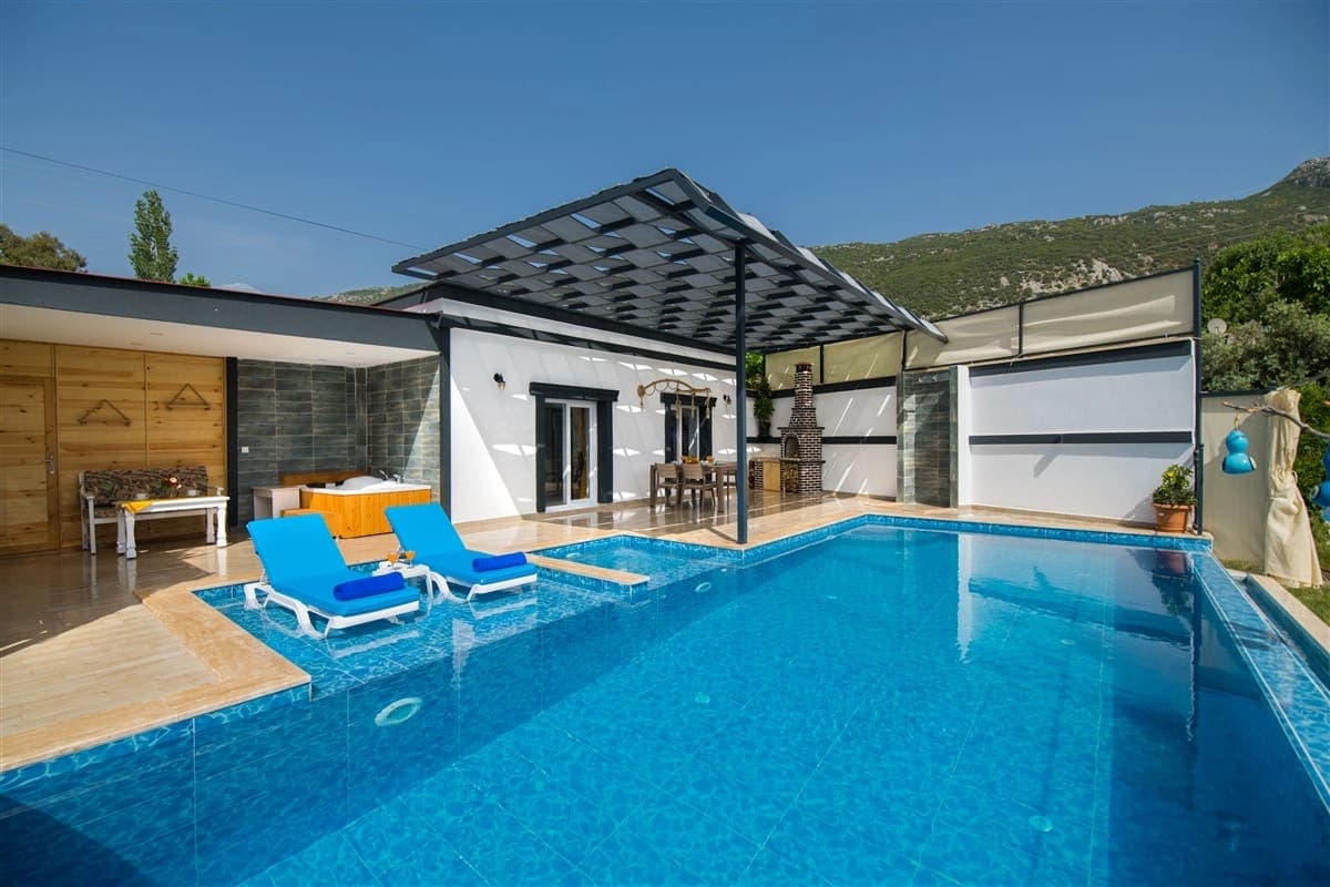 Güneşli günde mavi havuzlu ve şezlonglu villa bahçesi.