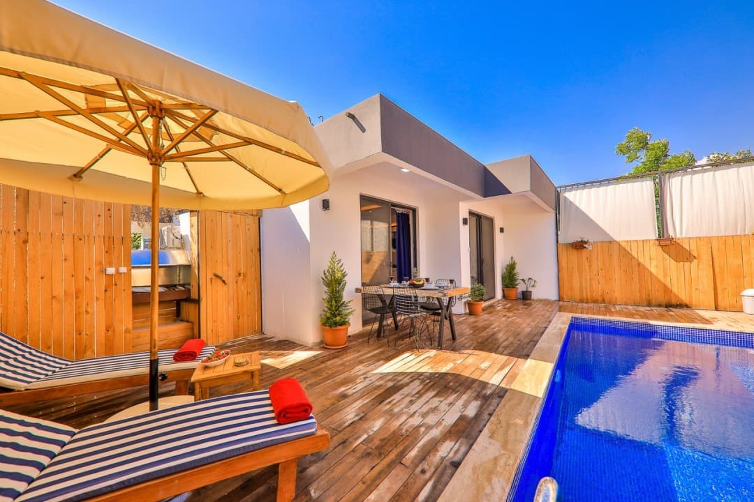 Havuz kenarında şezlonglar, şemsiye ve arka planda villa cephesi.