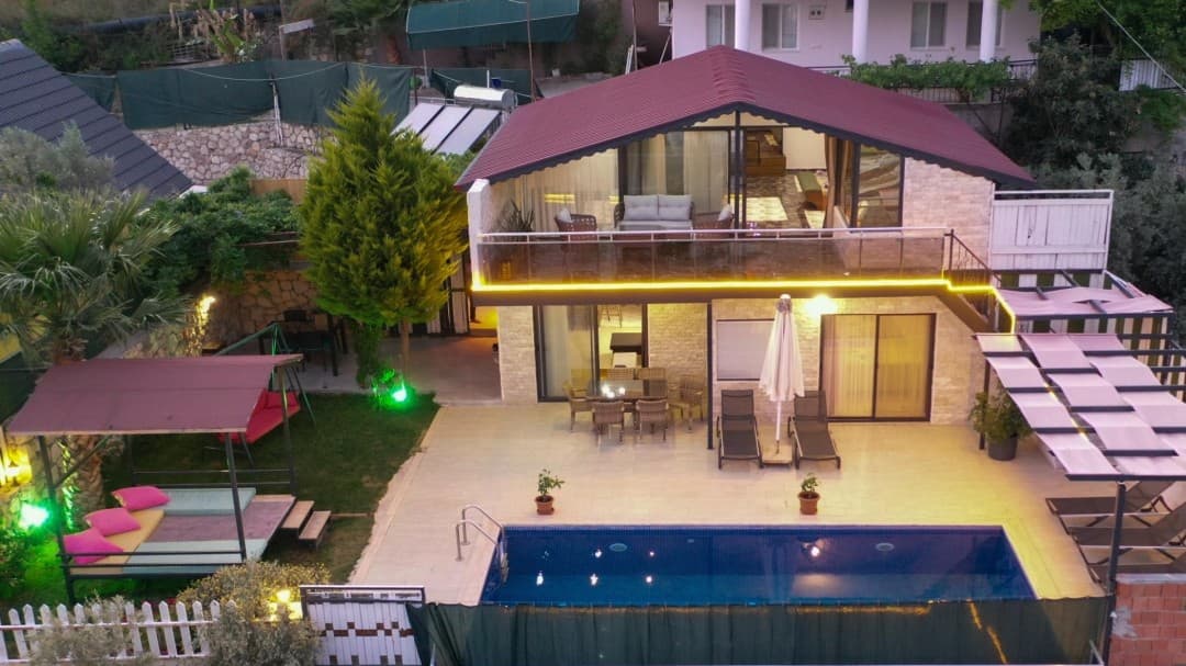 Akşam saatlerinde aydınlatılmış havuzu ve teras katı olan, bahçeli iki katlı villa.
