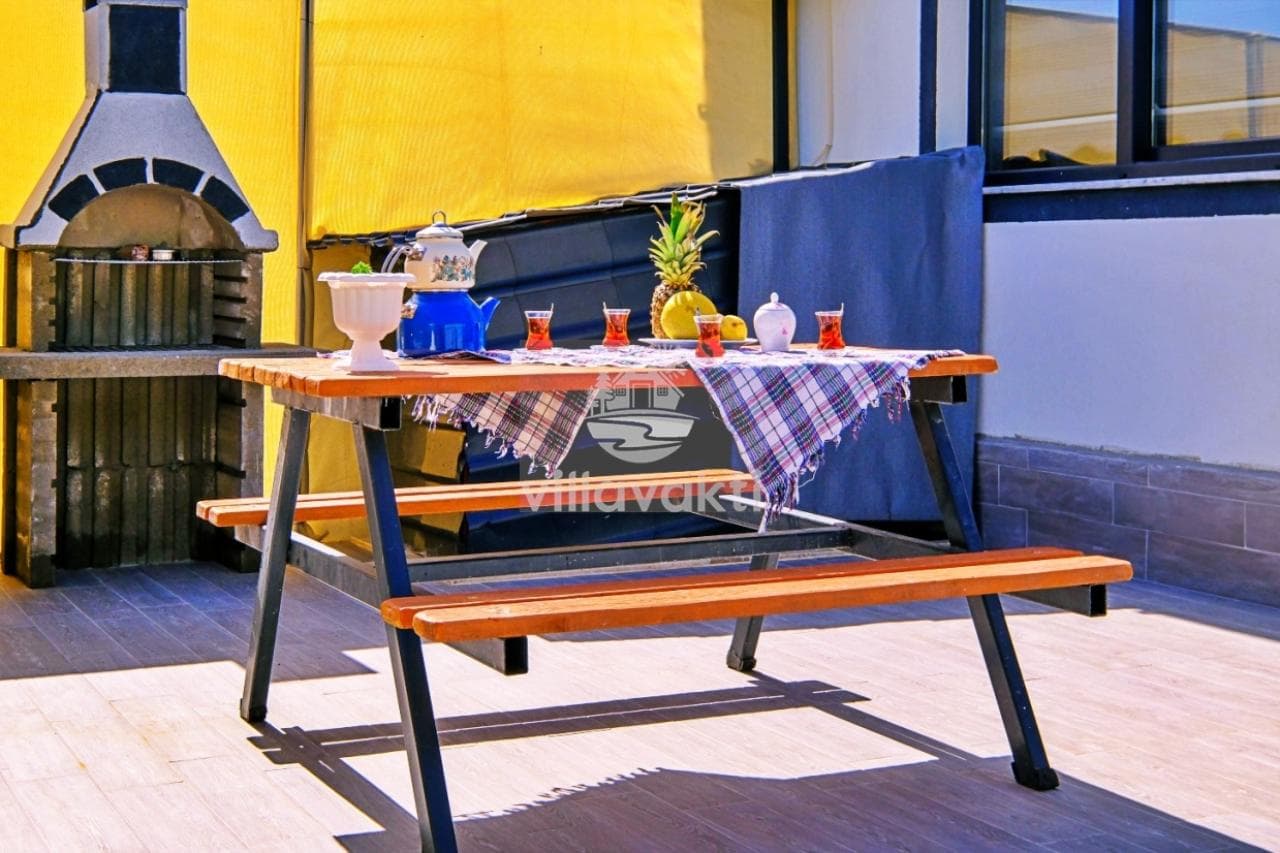 Bahçede piknik masası, çay bardağı ve taş barbekü yer alıyor.