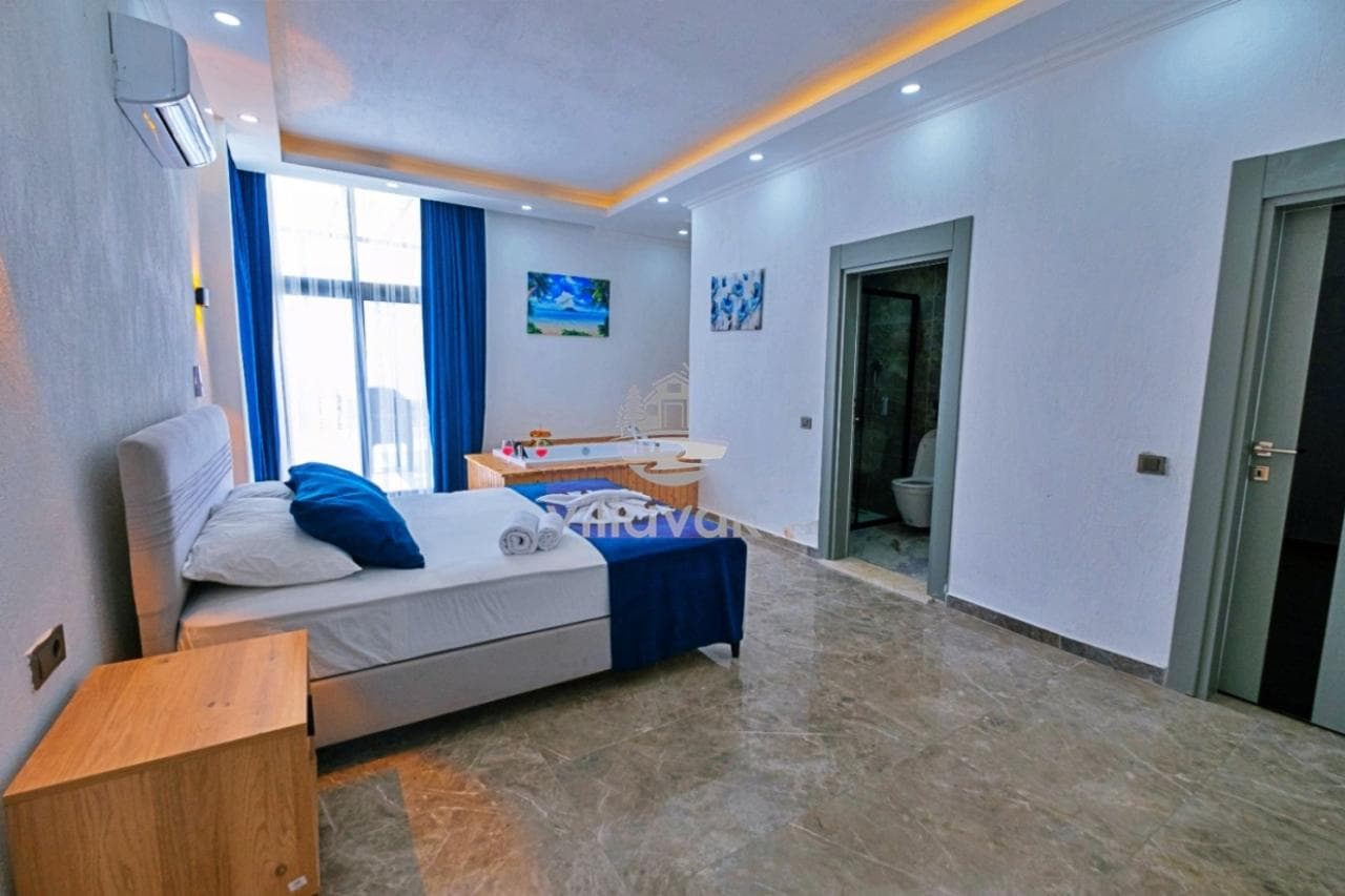 Mavi detaylı yatak odasında jakuzi, pencere ve banyo kapısı bulunuyor.