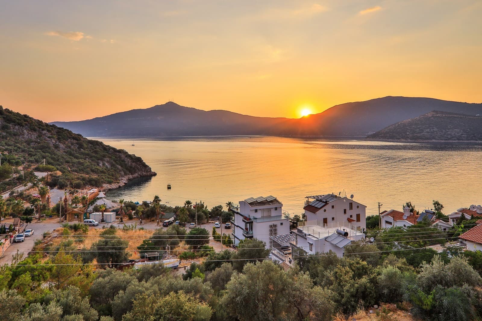 Dağlar ve deniz üzerinde batan güneşin oluşturduğu turuncu gün batımı manzarası.