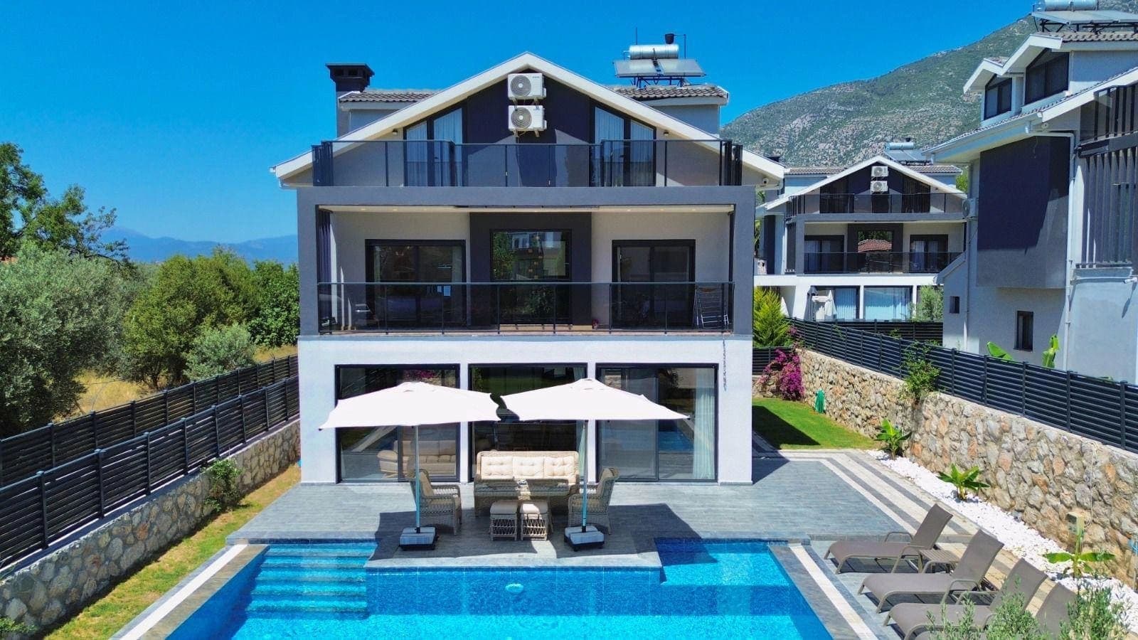 Geniş balkonlu çok katlı modern villa ve önünde havuz ile oturma grubu.