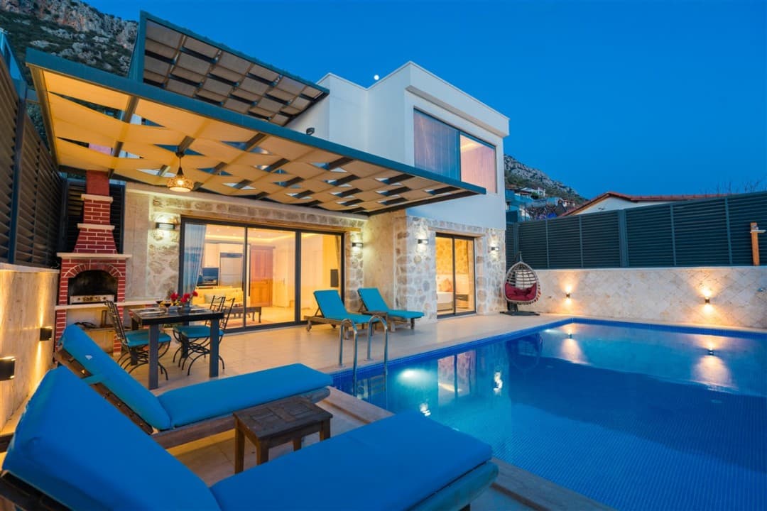 Akşam vakti havuz başı, şezlonglar ve pergolalı yemek alanı olan modern villa.