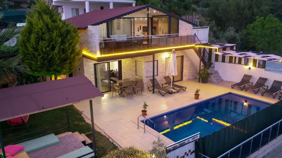 Gece aydınlatmalı iki katlı villanın havuzu, şezlongları ve oturma alanı.