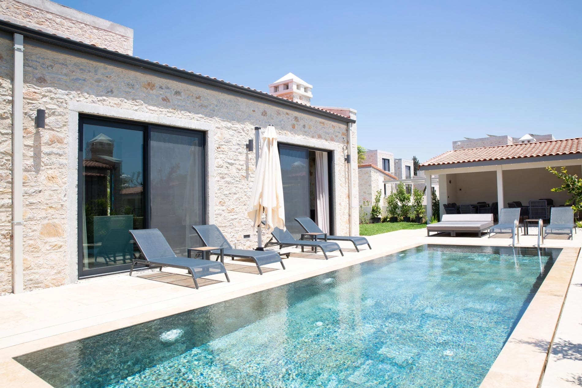 Açık havuz kenarında şezlonglar ve şemsiye bulunan taş villa dış cephesi