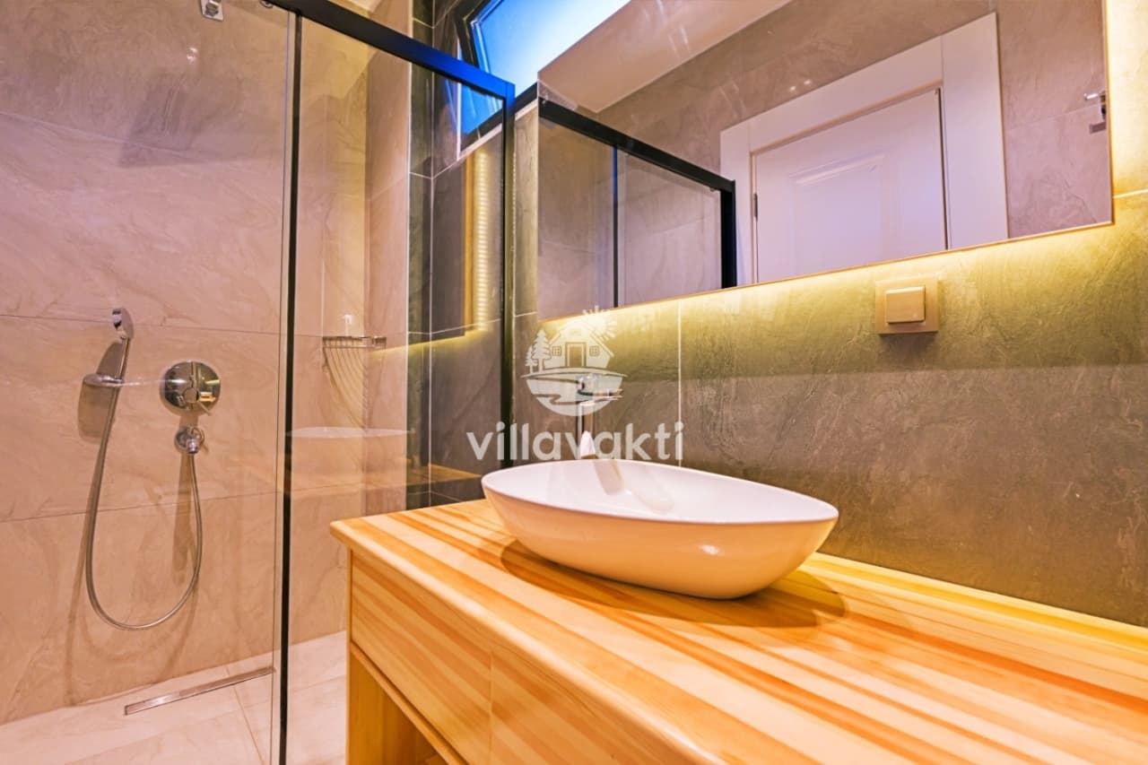 Ahşap tezgah üzerinde oval lavabo ve camlı duş kabini bulunan banyo