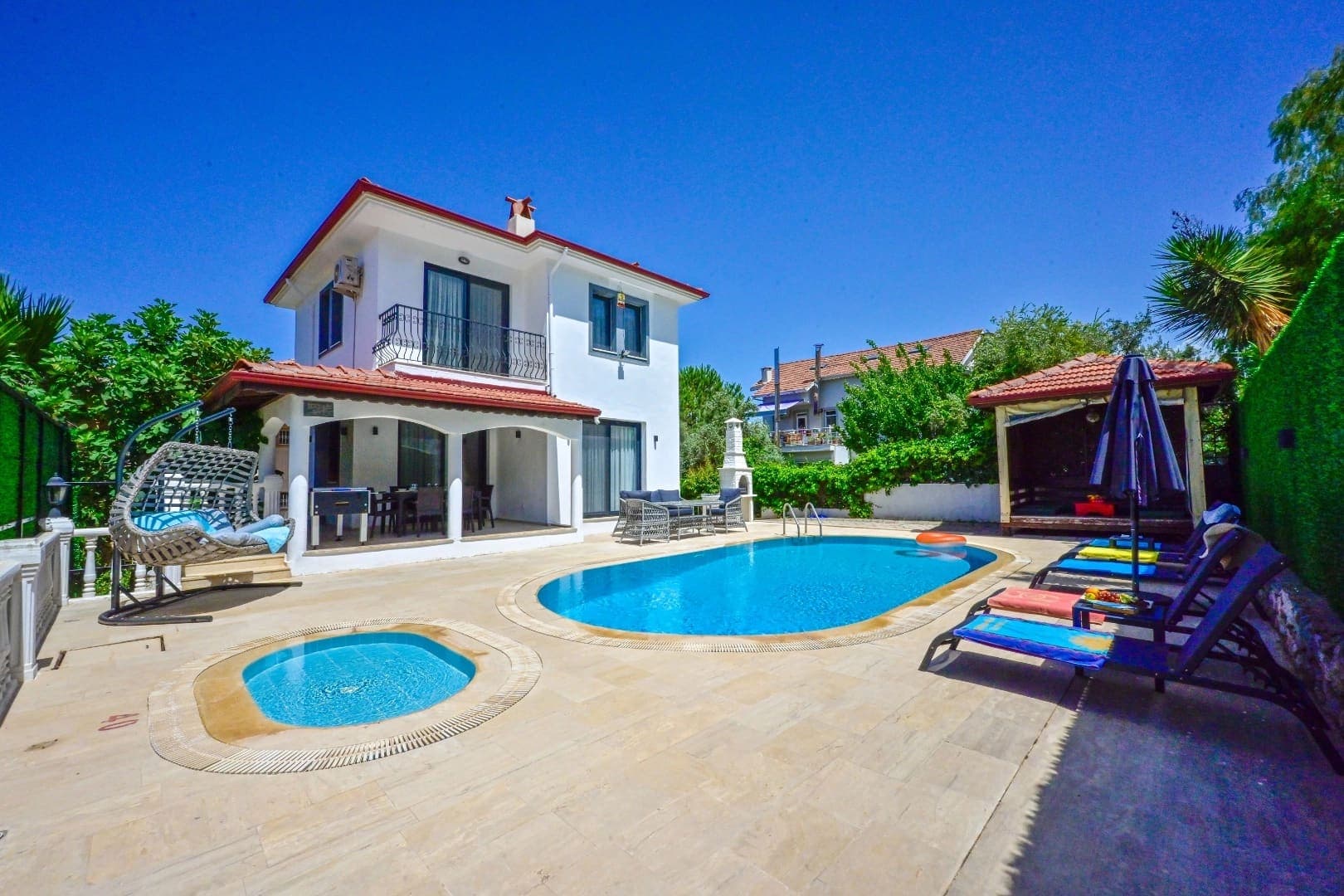 Bahçesinde yüzme havuzu ve şezlonglar bulunan beyaz iki katlı villa.