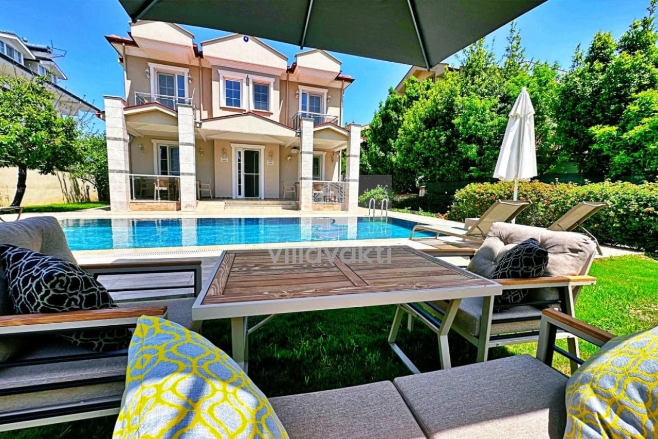 Bahçesinde havuz ve oturma grubu olan iki katlı bej villa.
