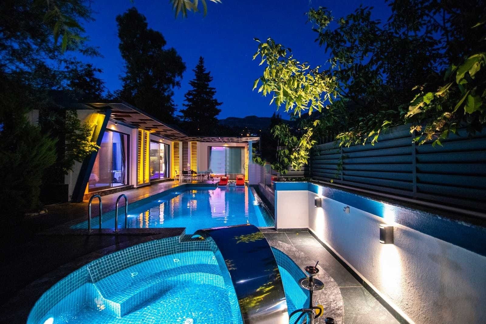 Gece aydınlatmalı, havuzlu ve jakuzili villa bahçesi.
