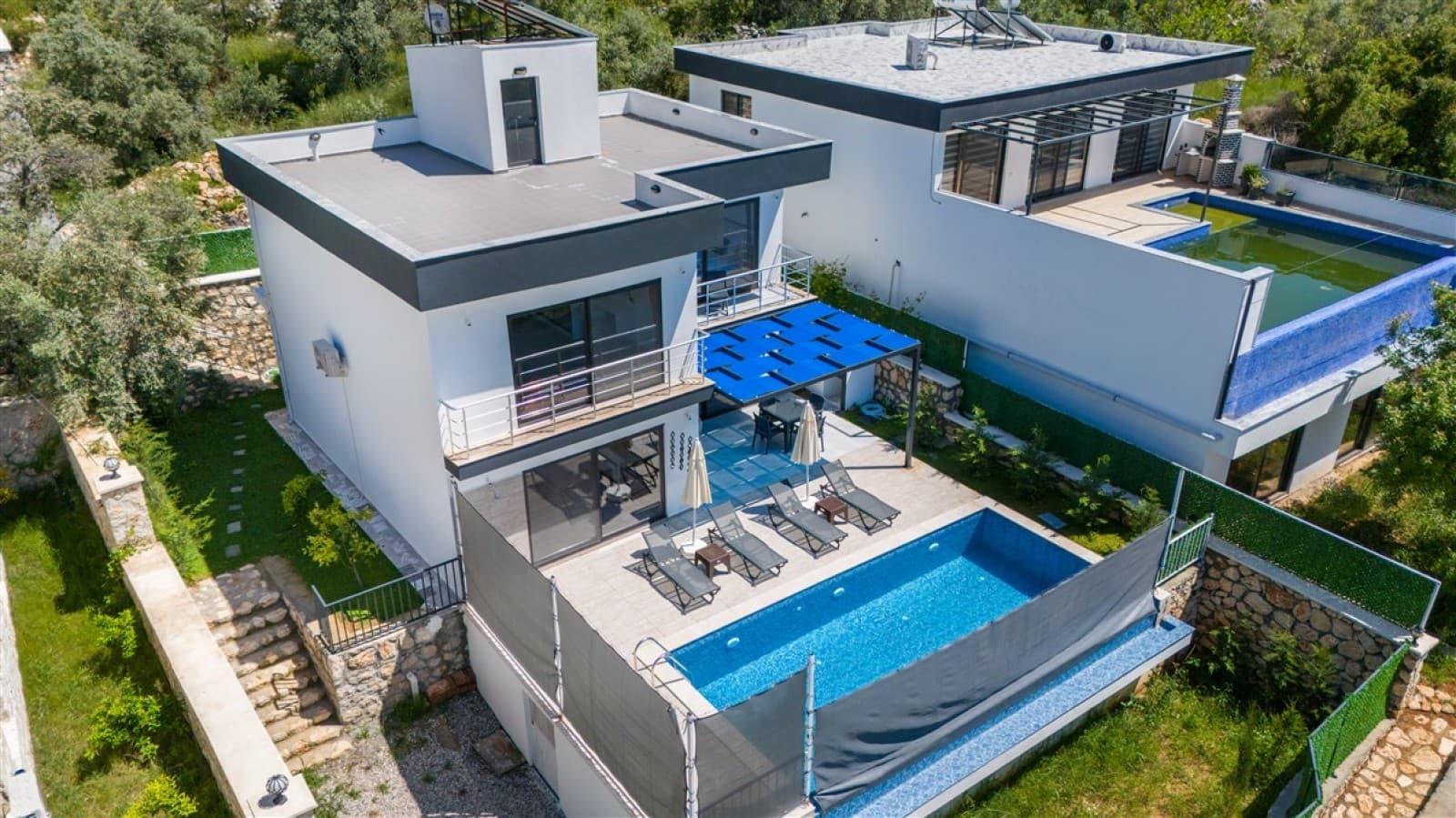 Mavi şezlonglu havuz başı ve beyaz dış cepheli iki katlı villa.